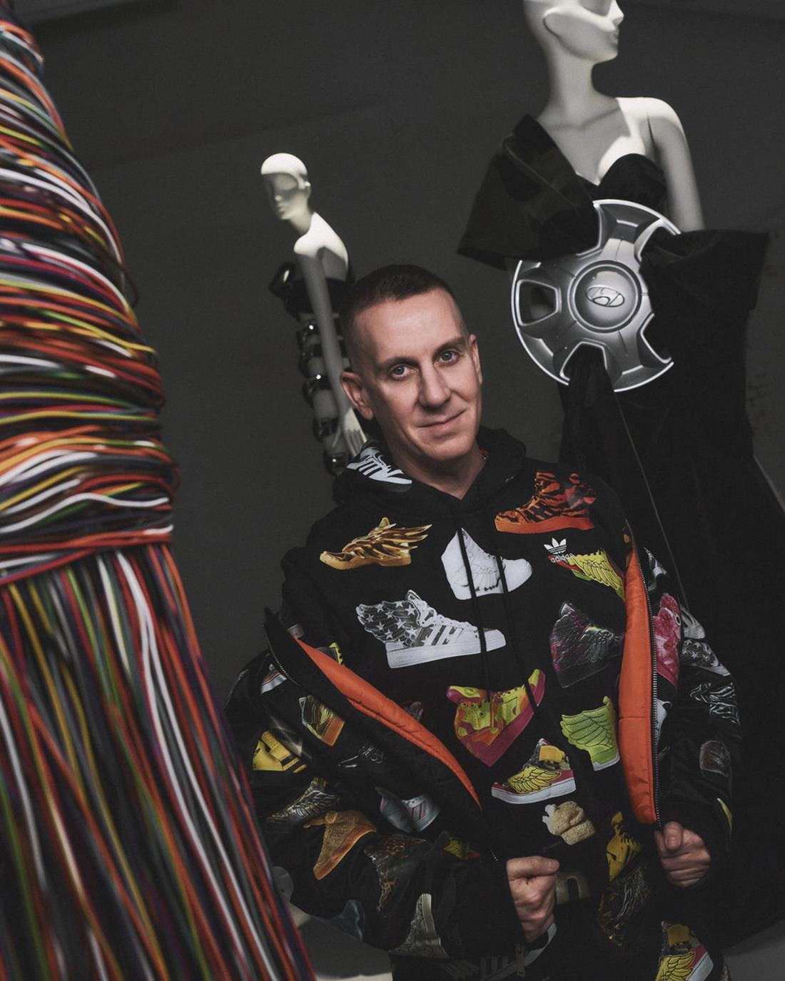 O estilista Jeremy Scott, um homem branco e de meia idade, de cabelo castanho curto. Eles está em uma sala em que é possível ver manequins, roupas e desenhos seus de looks que criou para a marca Hyundai. - Metrópoles