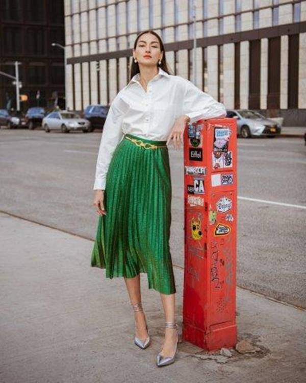 Na rua, mulher apoiada em caixa vermelha usa look com camisa branca e saia verde plissada - Metrópoles