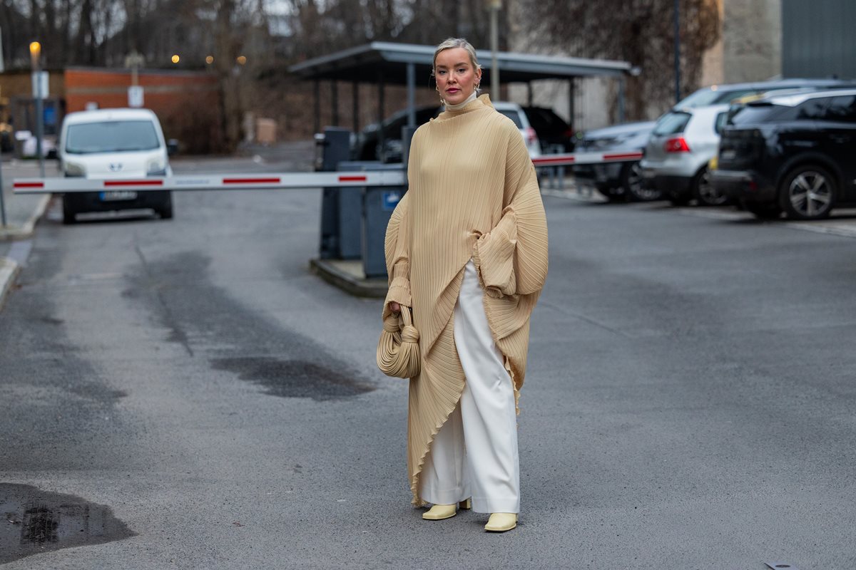 Mulher branca e jovem, de loiro liso, posa para foto em frente a um estacionamento em Berlim, na Alemanha. Ela usa um vestido longo bege, com tecido plissado, e calça ampla branca. - Metrópoles