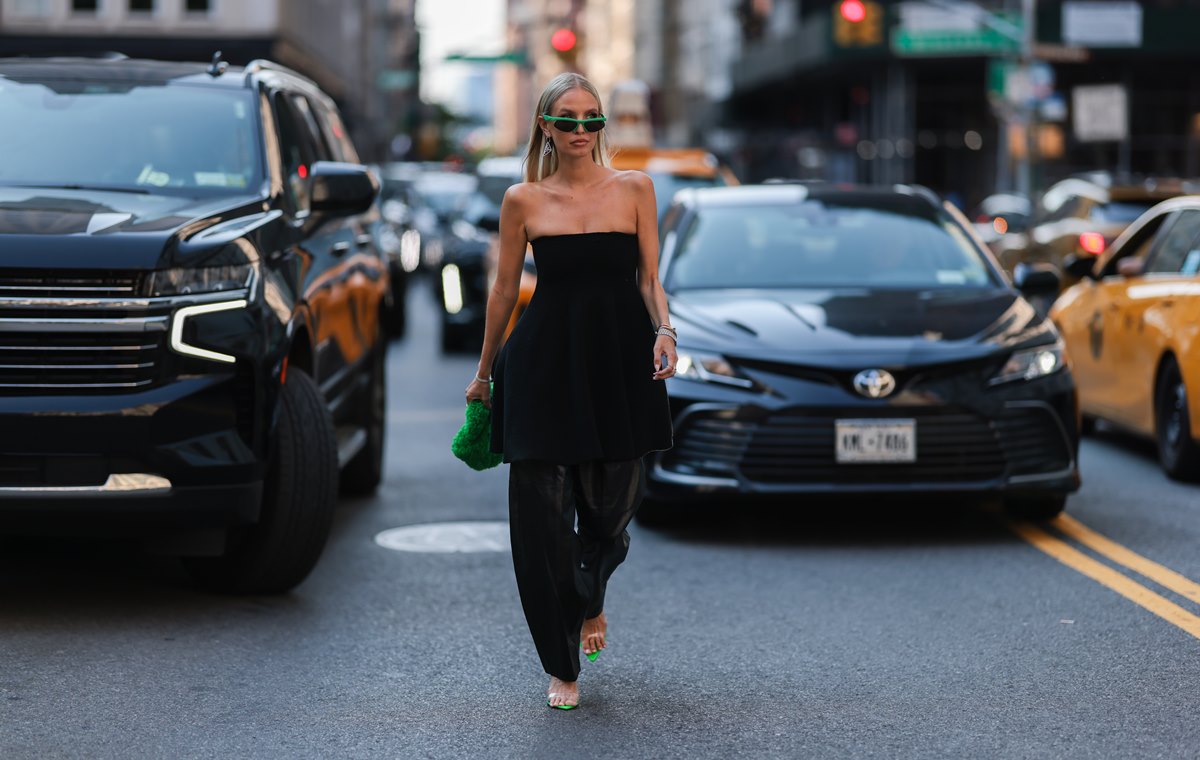 Mulher branca e jovem, de loiro liso, posa para foto andando na rua em Nova York. Ela usa um vestido curto e uma calça, tudo na cor preta. - Metrópoles