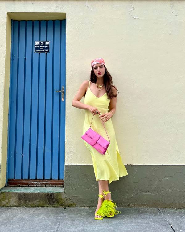 Mulher branca usa vestido amarelo, sapato verde com plumas e lenço rosa no cabelo - Metrópoles 