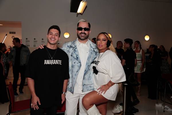 Três pessoas posando para foto. Elas estão se abraçando dentro do backstage de um desfile - Metrópoles