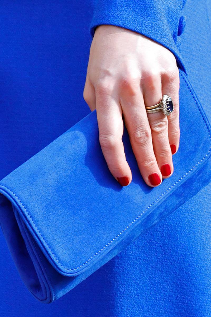 Foto colorida de mulher branca com esmalte na cor vermelha. Ela segura uma bolsa azul royal - Metrópoles