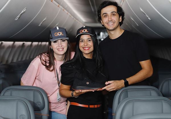 Três pessoas em aeronave. Eles estão posando para a foto segurando um par de tênis - Metrópoles