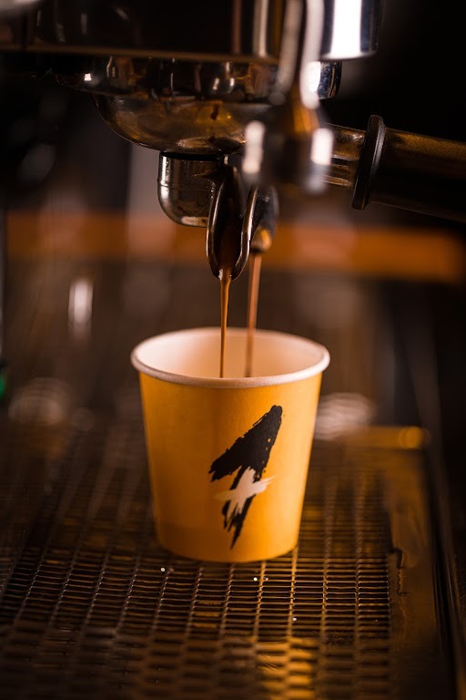 Foto de um copo de papel embaixo de uma máquina de café enquanto a bebida é colocada dentro dele