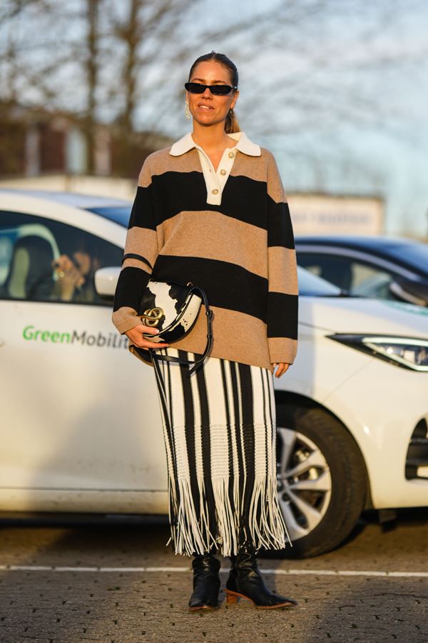 Mulher parada em frente a um carro. Ela está segurando uma bolsa de mão - Metrópoles