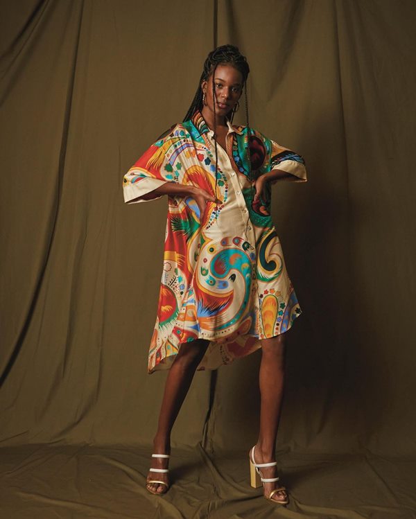 Na imagem com cor, uma mulher negra de cabelos pretos presos usando um vestido estampado colorido - Metrópoles