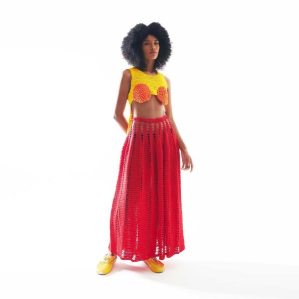 Na imagem com cor, mulher negra com cabelos pretos usando um conjunto cropped e saia rosa e amarelo de crochê - Metrópoles