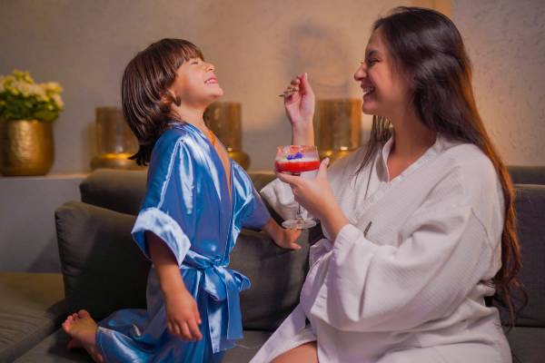 Fotografia colorida mostrando mãe dando gelatina para o filho e ambos usando roupão-Metrópoles