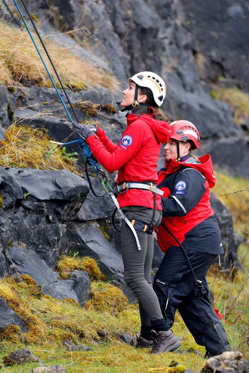 Foto colorida de mulher branca, com casaco vermelho e capacete branco, prestes a fazer escalada com equipamentos de segurança - Metrópoles