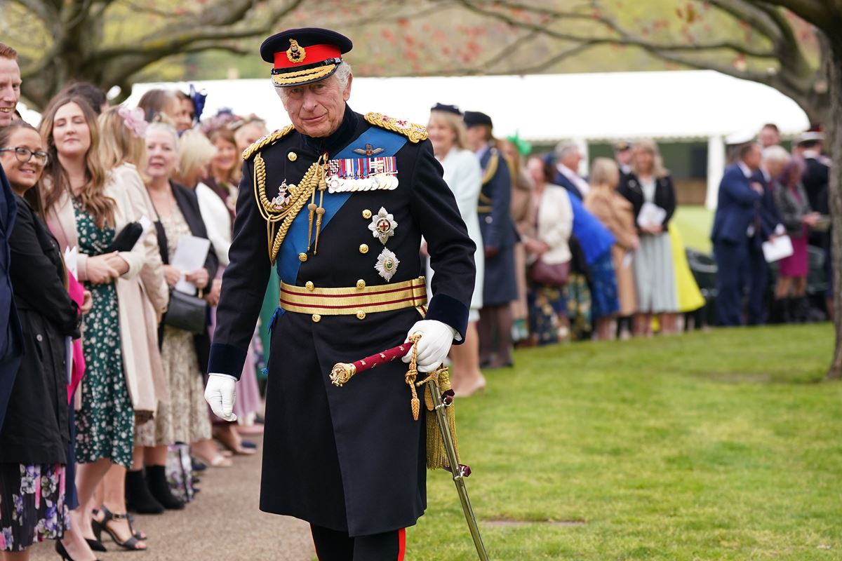 Foto colorida de homem idoso e branco andando em um gramado. Ele usa trajes militares britânicos. Há pessoas ao redor dele - Metrópoles