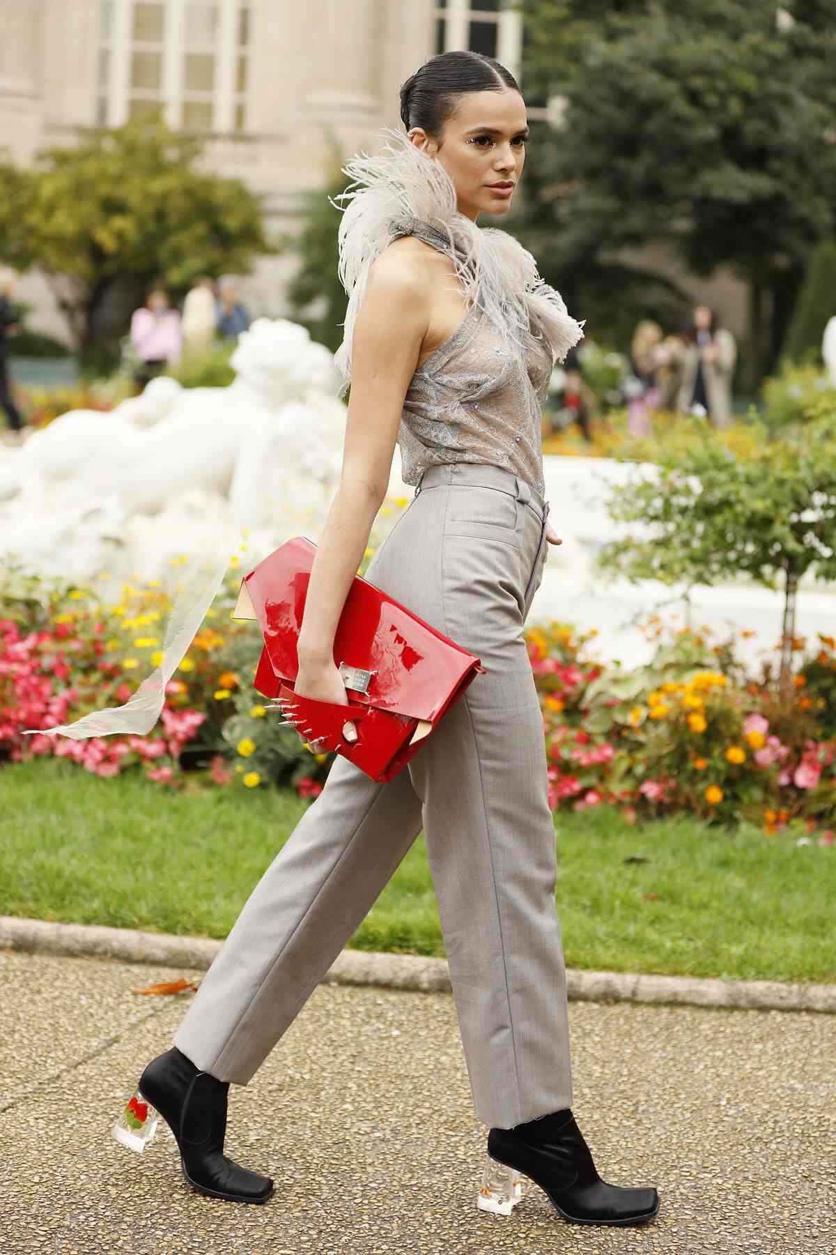 Na imagem com cor, uma mulher branca, com cabelos castanhos e presos, andando enquanto usa uma blusa e calça cinza - Metrópoles