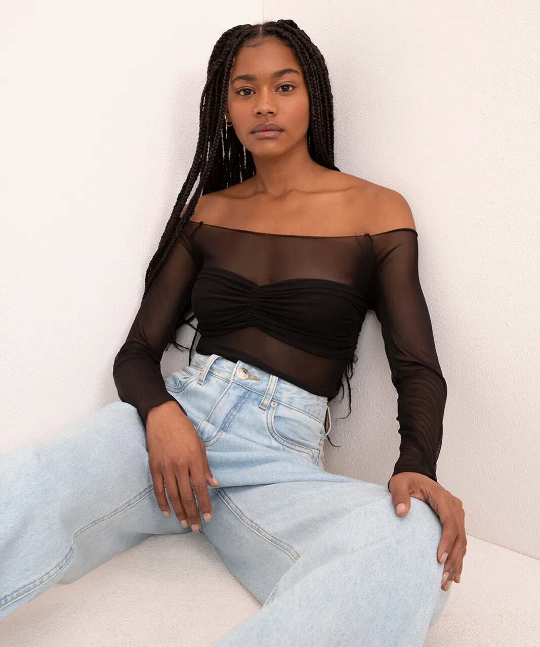 Na imagem com cor, uma mulher negra de cabelos pretos soltos usando uma blusa preta com detalhes de transparência e calça jeans - Metrópoles