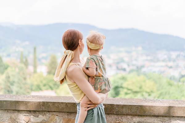 Jovem mulher branca com um bebê nos braços contra o pano de fundo da paisagem natural italiana - Metrópoles