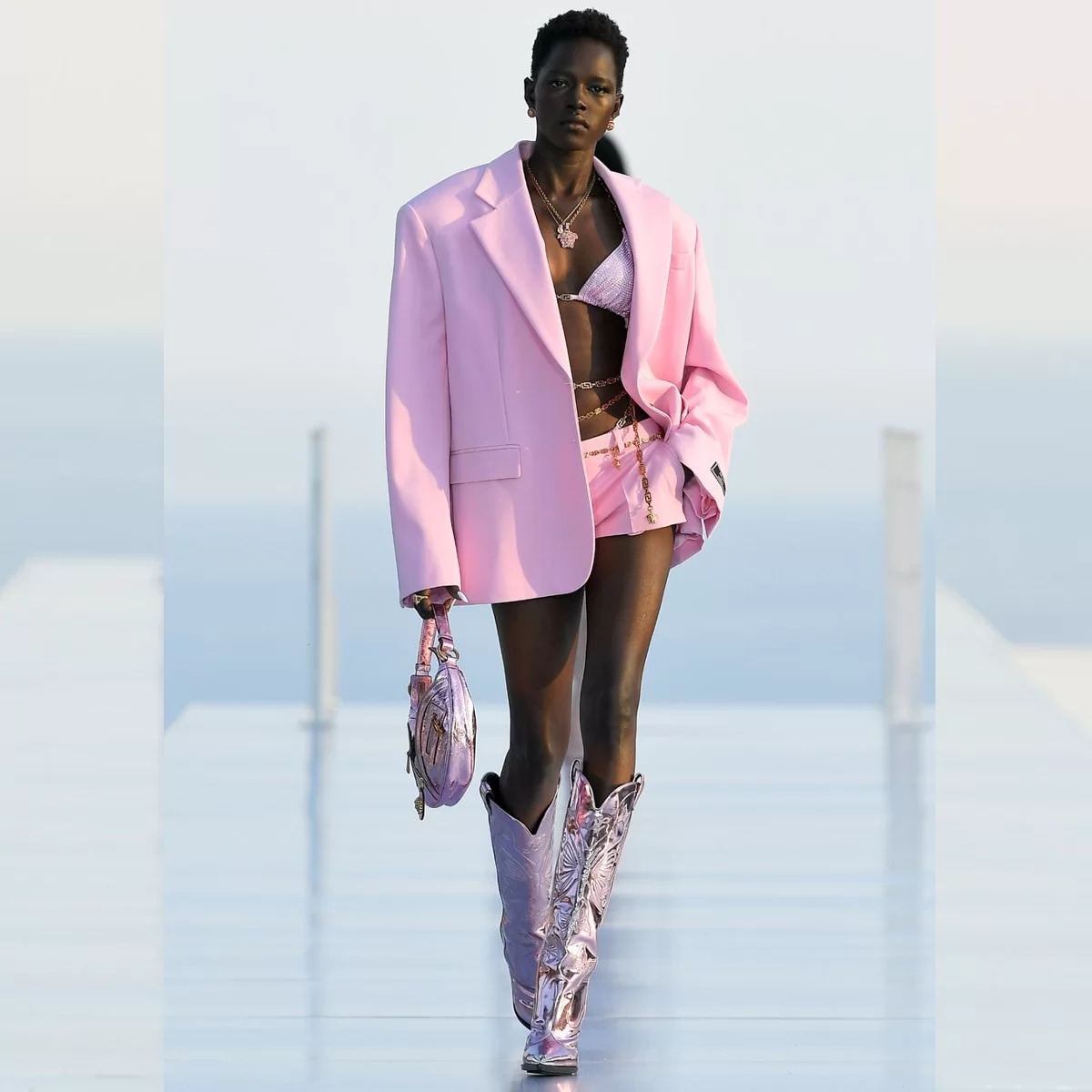 Na imagem com cor, uma mulher negra de cabelos pretos presos desfilando com uma roupa rosa - Metrópoles