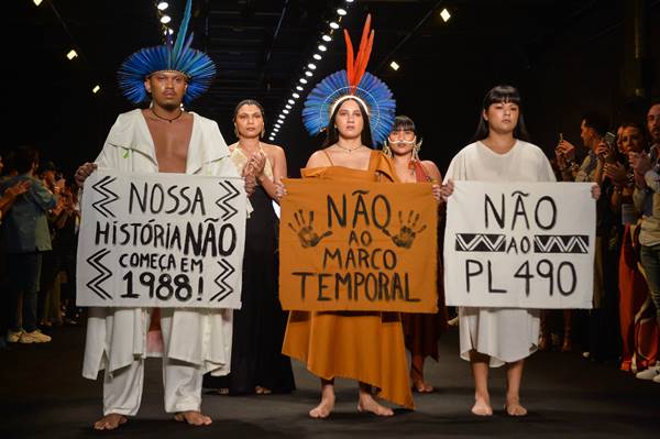 Indígenas protestam em desfile contra o marco temporal. Na imagem, seguram cartazes - Metrópoles