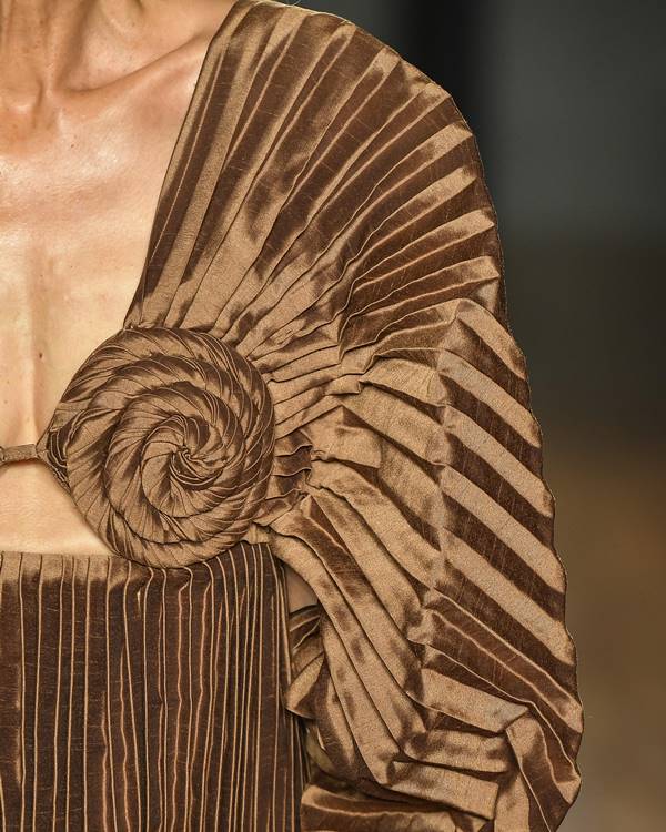 Detalhes plissados em roupa marrom cintilante - Metrópoles