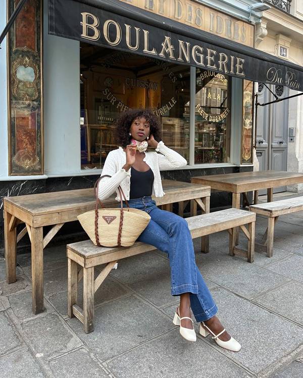 Na imagem com cor, uma mulher negra sentada com uma blusa preta, casaco branco e calça jeans - Metrópoles