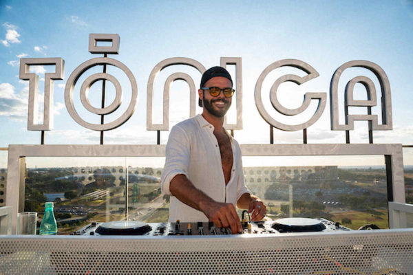 Na imagem com cor, uma homem branco DJ tocando usando uma camisa branca - Metrópoles 