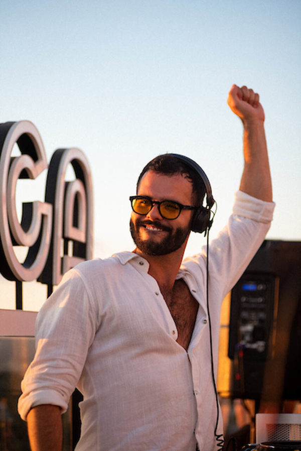 Na imagem com cor, uma homem branco DJ dançando usando uma camisa branca - Metrópoles 