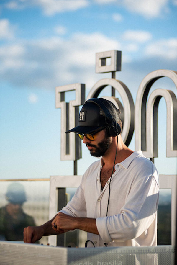 Na imagem com cor, uma homem branco DJ tocando usando uma camisa branca - Metrópoles 