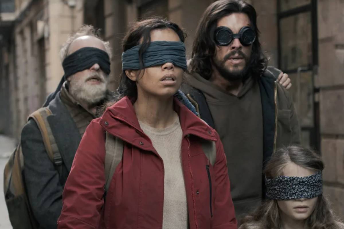 Imagem colorida do filme Bird Box Barcelona, composta por dois homens brancos e uma mulher negra, todos estão vendados - Metrópoles