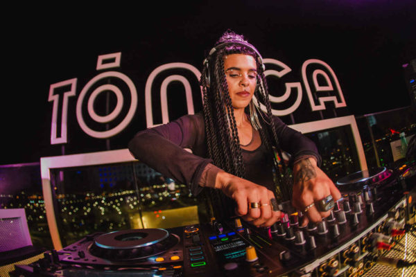 Na imagem com cor, uma mulher negra DJ tocando com fones de ouvido - Metrópoles