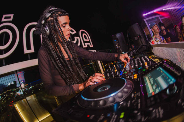 Na imagem com cor, uma mulher negra DJ tocando com fones de ouvido - Metrópoles