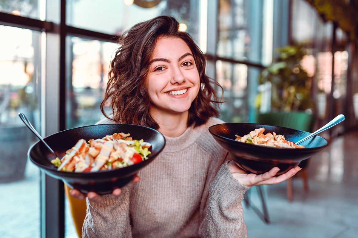 Foto colorida de mulher branca com dois bowls cada um em uma mão - Metrópoles