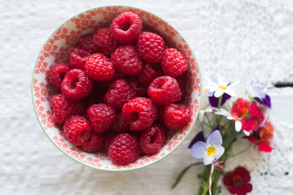 Foto colorida de framboesa em bowl ao lado de flores - Metrópoles