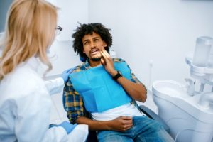 Foto mostra uma dentista atendendo um homem vestido com um avental e sentado em uma cadeira de dentista - Metrópoles