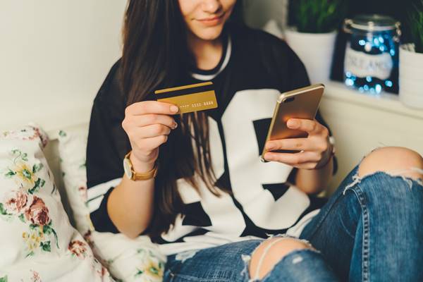 Adolescente fazendo compra on-line. Ela segura um cartão de crédito e um celular - Metrópoles