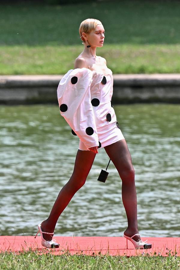 Em desfile no Grande Canal do Palácio de Versalhes, modelo usa vestido branco com bolinhas pretas, além de meia-calça preta - Metrópoles