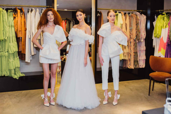 Na imagem com cor, três mulheres brancas, posando em uma loja com vestidos em branco- Metrópoles