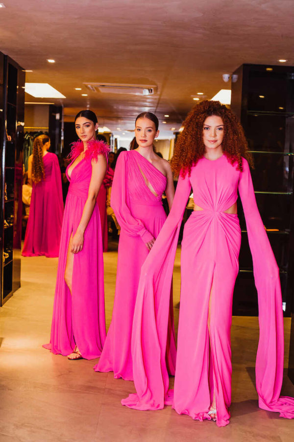 Na imagem com cor, três mulheres brancas, posando em uma loja com vestidos em rosa- Metrópoles