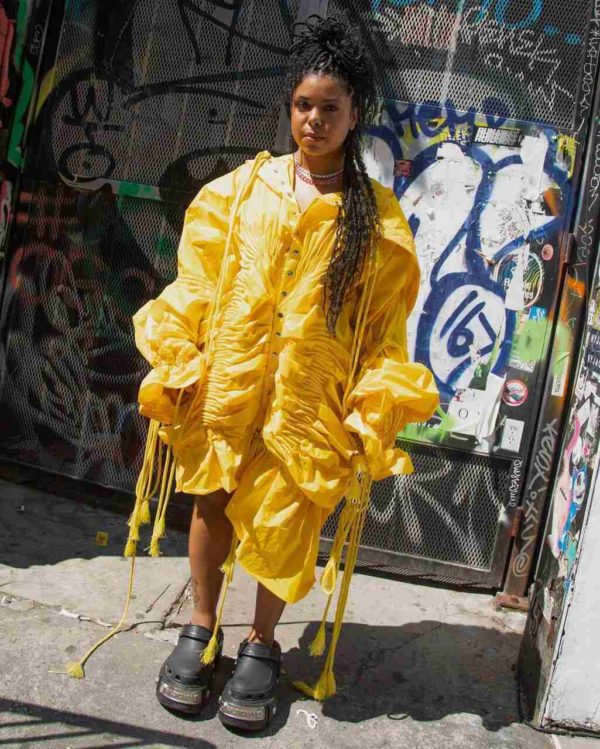 Na imagem com cor, uma mulher negra em pé na rua com um vestido amarelo - Metrópoles