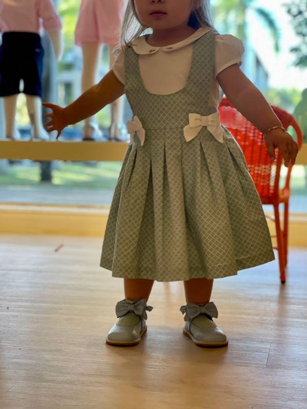 Criança usa vestido rodado. Nos pés, calçado infantil azul de couro com laço - Metrópoles