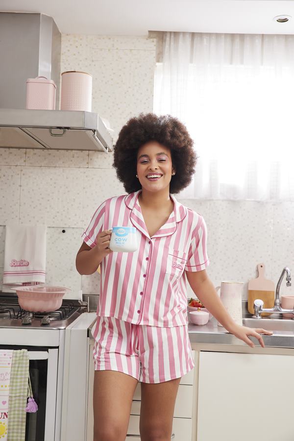 Mulher apoiada na bancada da cozinha. Ela está segurando uma xícara e sorrindo para a foto - Metrópoles