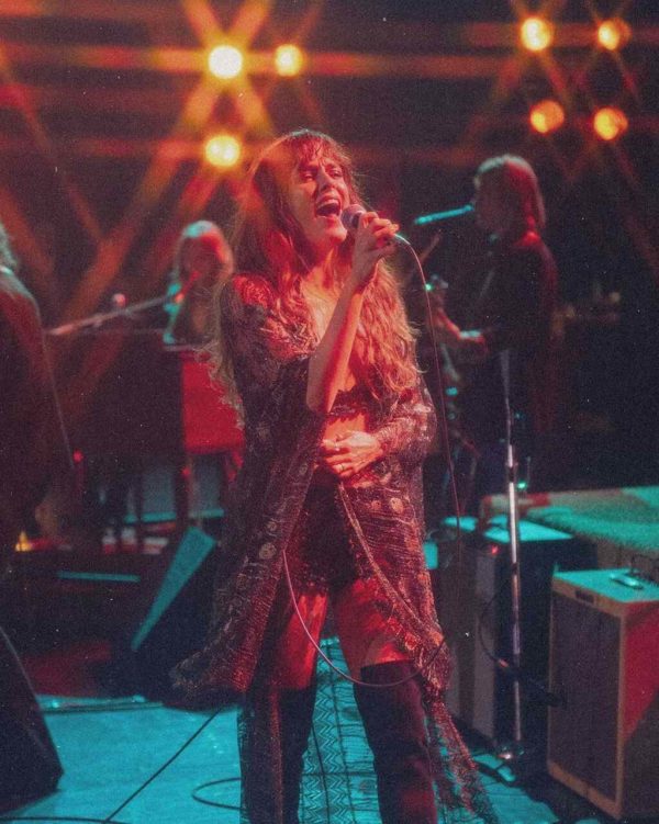 Na imagem com cor, uma mulher branca ruiva em um palco cantando - Metrópoles