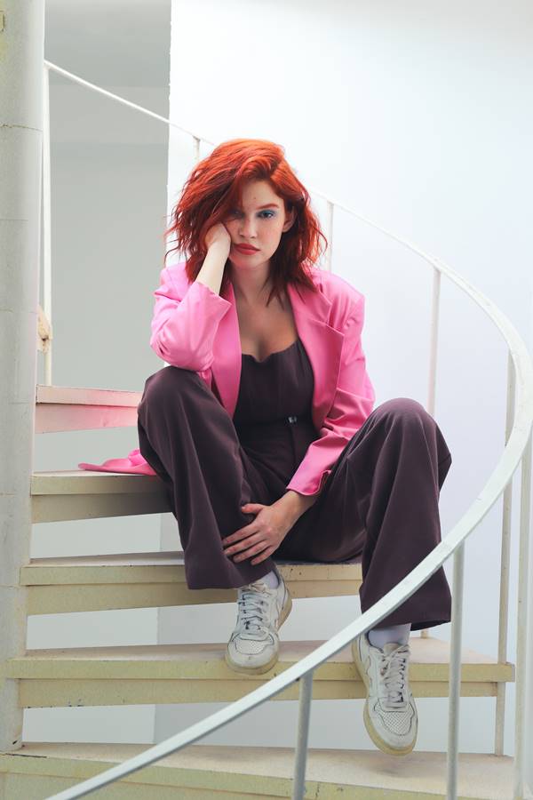 Mulher ruiva sentada em escada usando look marrom de alfaiataria com blazer rosa - Metrópoles