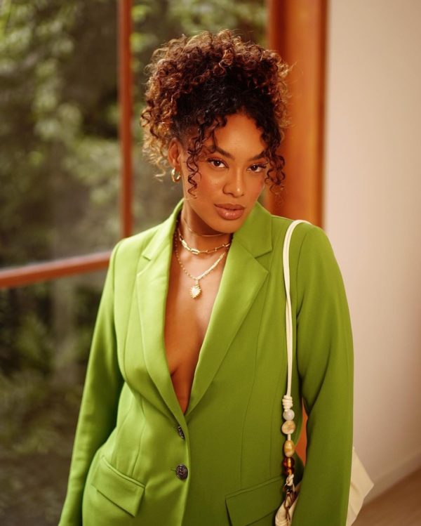 Na imagem com cor, uma mulher negra com os cabelos cacheados presos de blazer verde