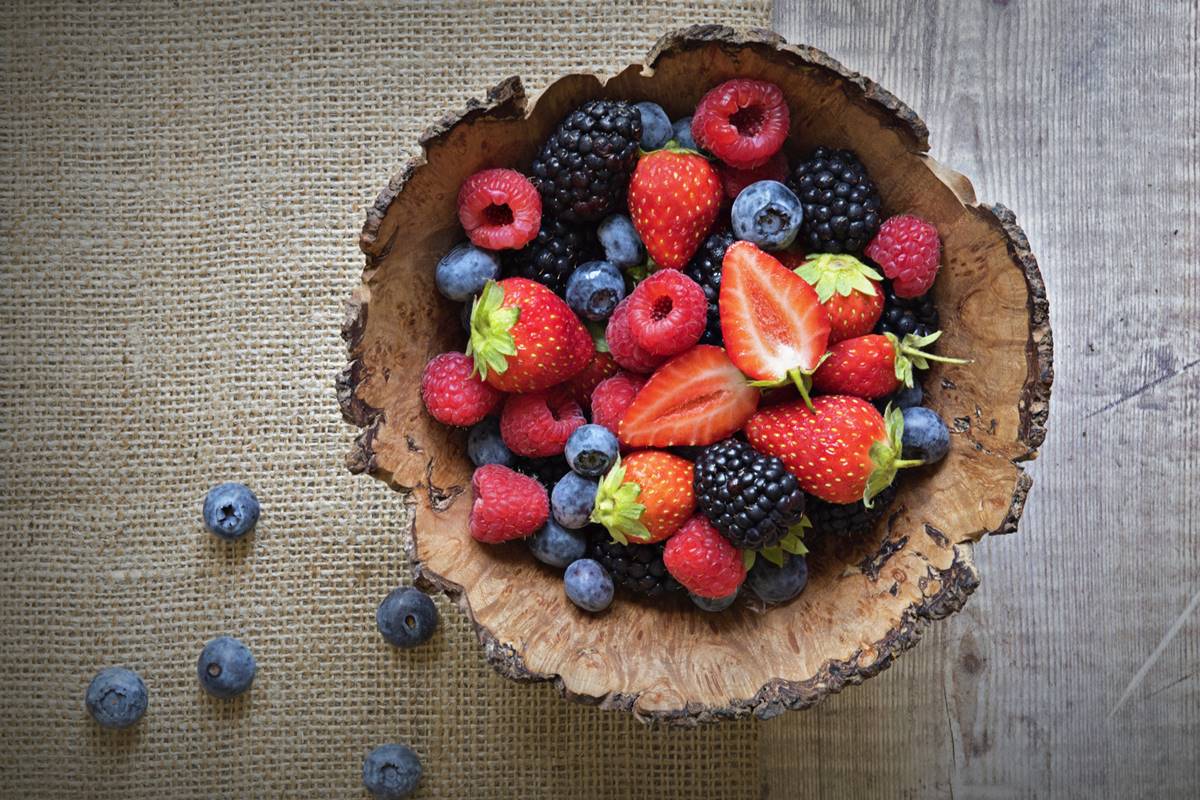 Foto colorida de vasilha de madeira com frutas, a exemplo de morango, mirtilo, amora e framboesa, dentro - Metrópoles