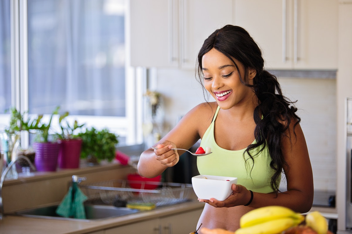 Mulher negra sorrindo comendo frutas em um recipiente - Metrópoles