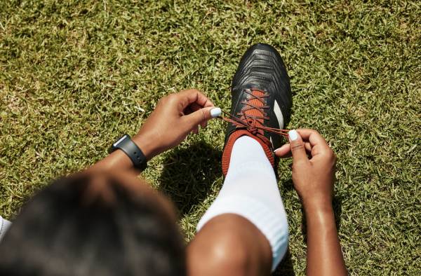 Fotografia colorida mostrando jogadora de futebol amarrando as chuteiras-Metrópoles