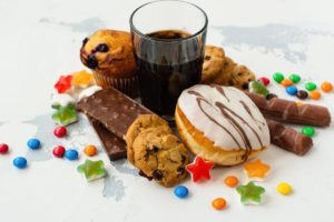 Foto colorida de balinhas, barras de chocolate, copo de refrigerante, donuts, cookies e muffins - Metrópoles