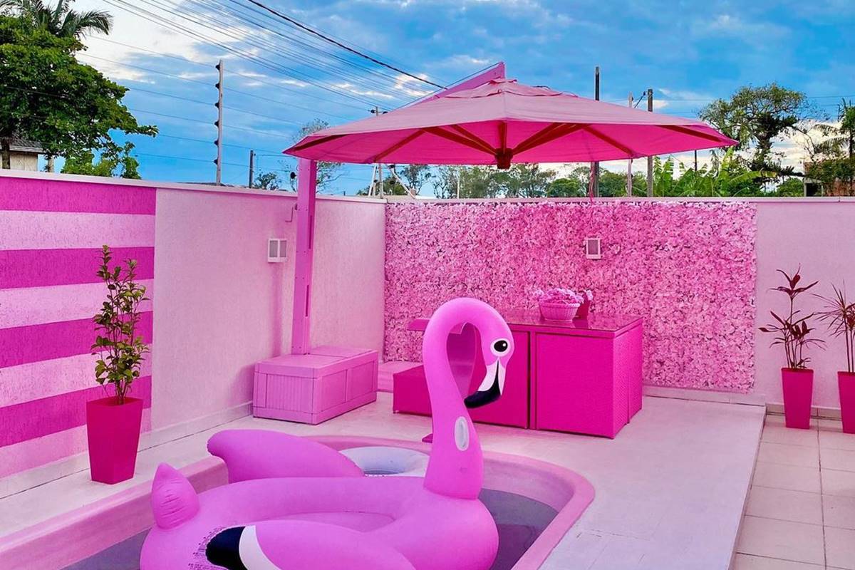 Foto colorida de espaço ao ar livre com piscina, boia de flamingo e guarda-sol cor-de-rosa - Metrópoles