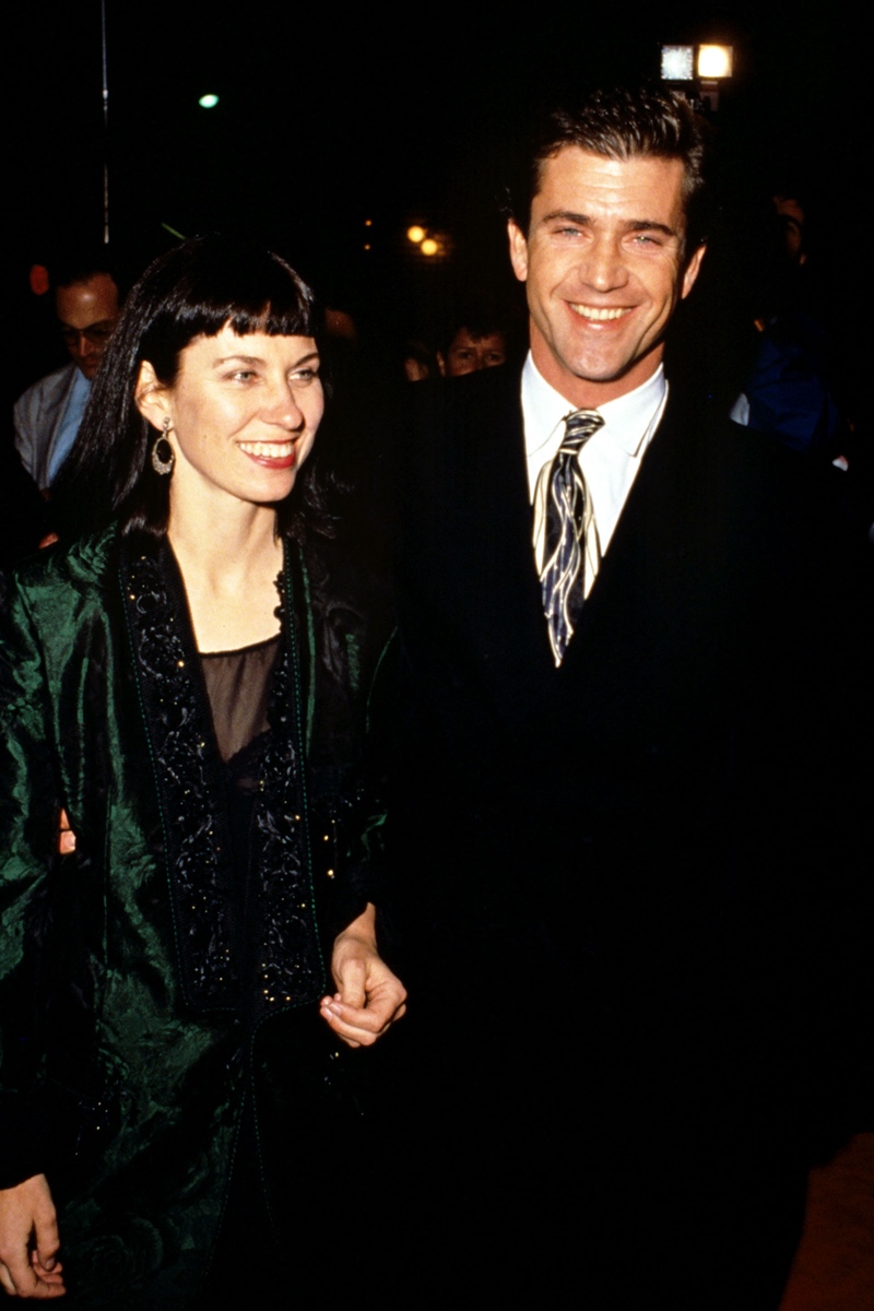 Foto colorida. Robyn Moore and Mel Gibson são um ex-casal. Ambos são brancos. Ela tem cabelo curto, preto e liso. Ele está de terno preto, sorrindo e segurando na mão da ex-esposa - Metrópoles