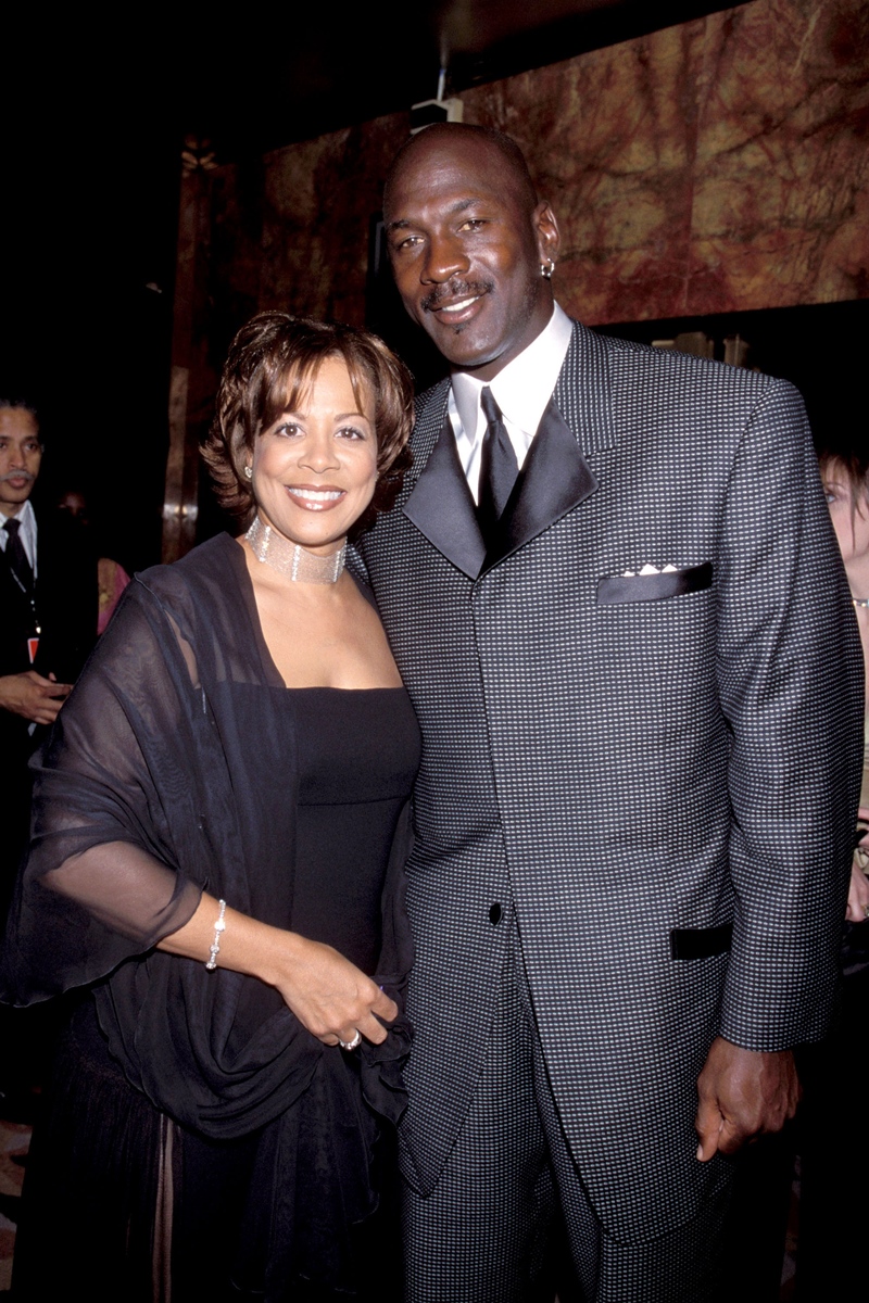 Foto colorida. Michael e Juanita Jordan são um ex-casal. Ela é negra, cabelos lisos castanhos, curto e está usando um vestido preto. Ele é negro, careca e está usando um terno cinza - Metrópoles