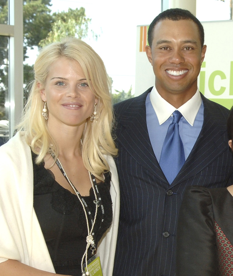Foto colorida. Tiger Woods e Elin Nordegren são ex-marido e ex-mulher. Ele é negro, de cabelos pretos e está usando um terno preto, camisa e gravata azul. Ela é loira, cabelos lisos na altura dos ombros e está usando uma blusa preta e um sobretudo branco - Metrópoles