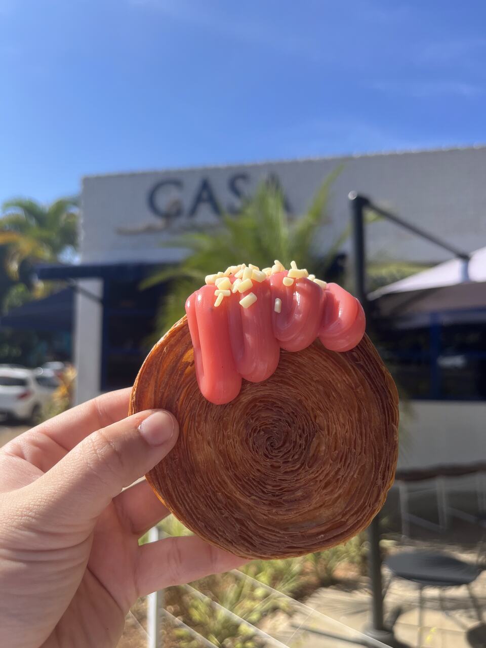 Na foto, uma pessoa segurando um doce circular com calda cor-de-rosa - Metrópoles